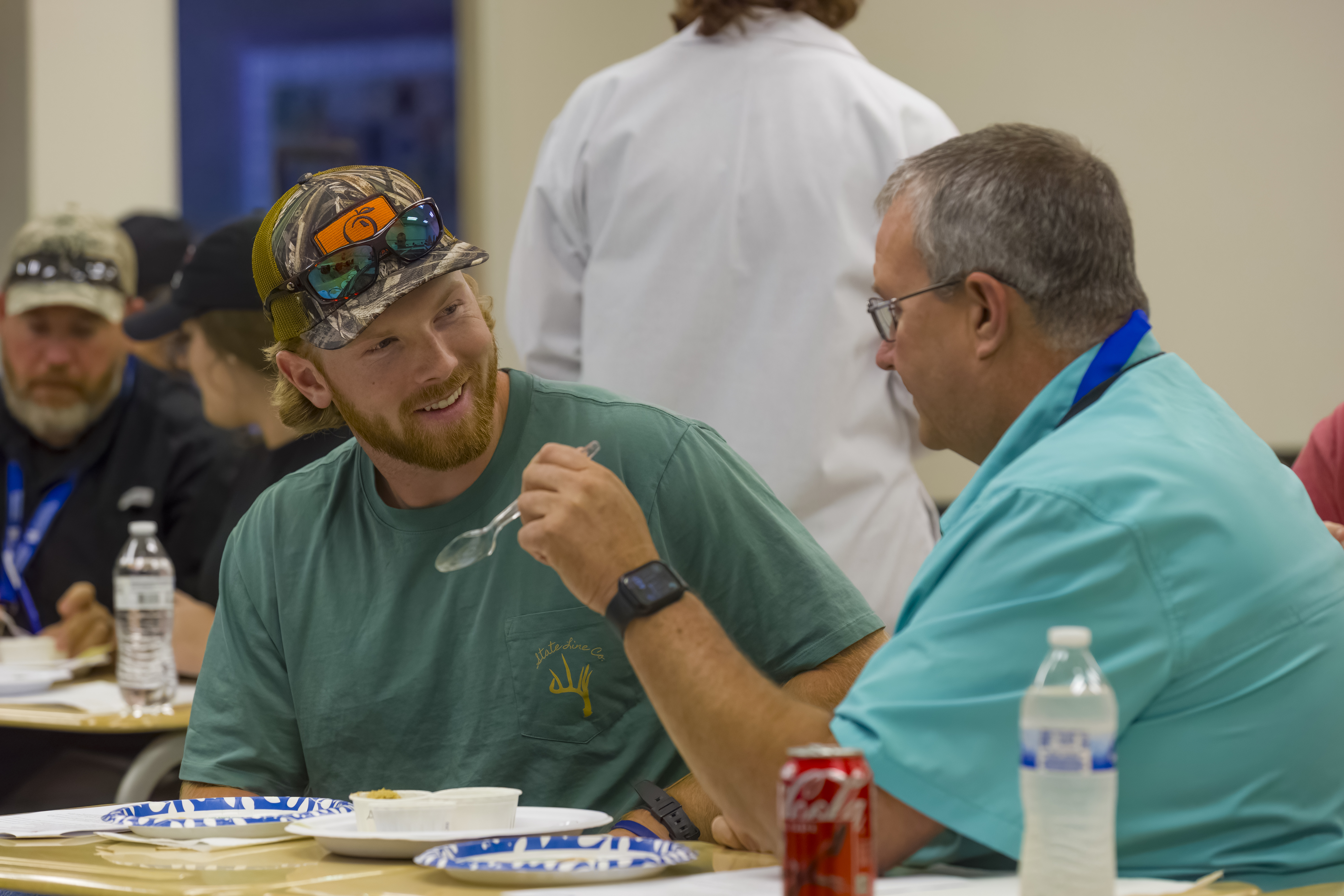 Two men talk as they try food samples. 