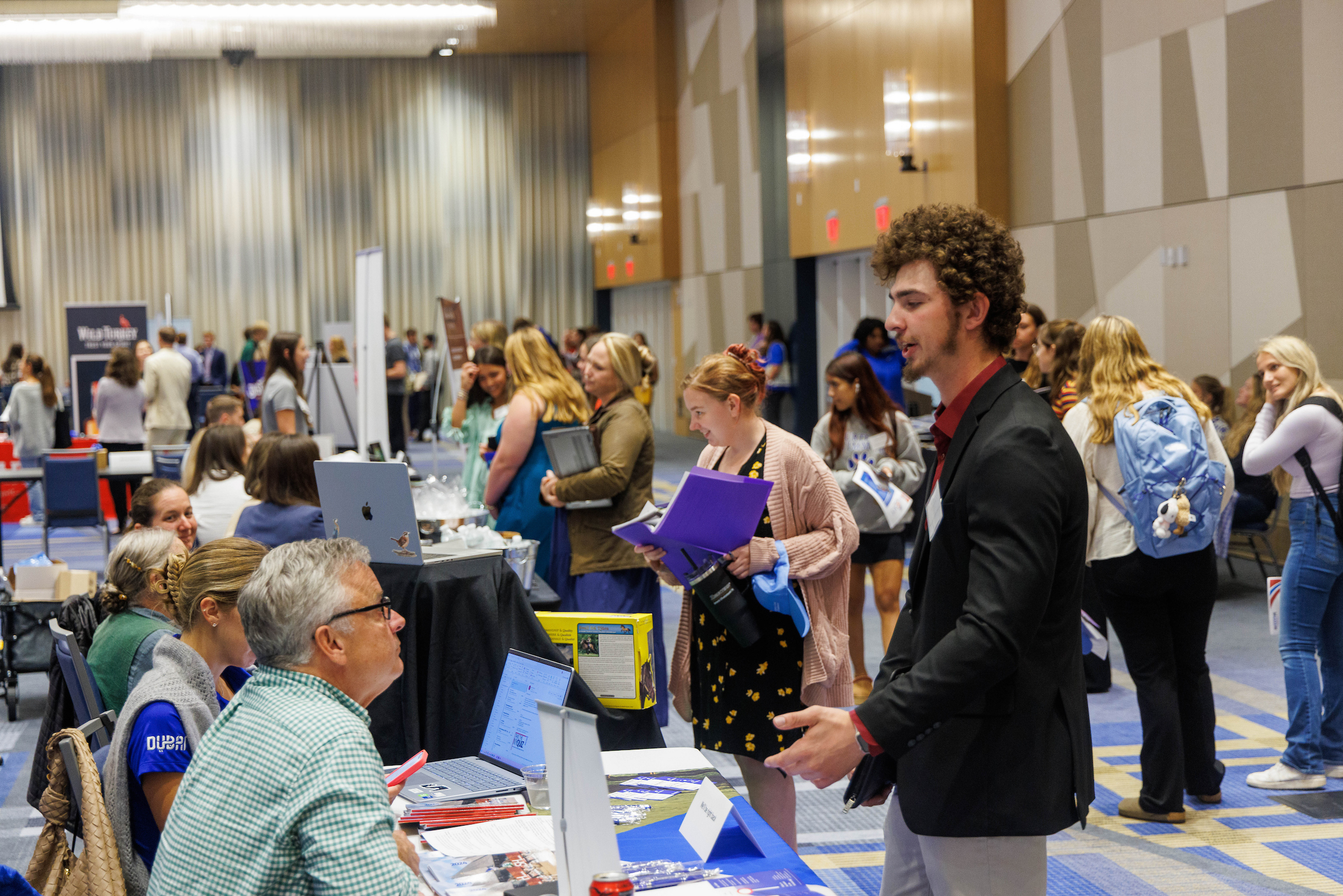 People talk to employers set up at tables at a career fair.