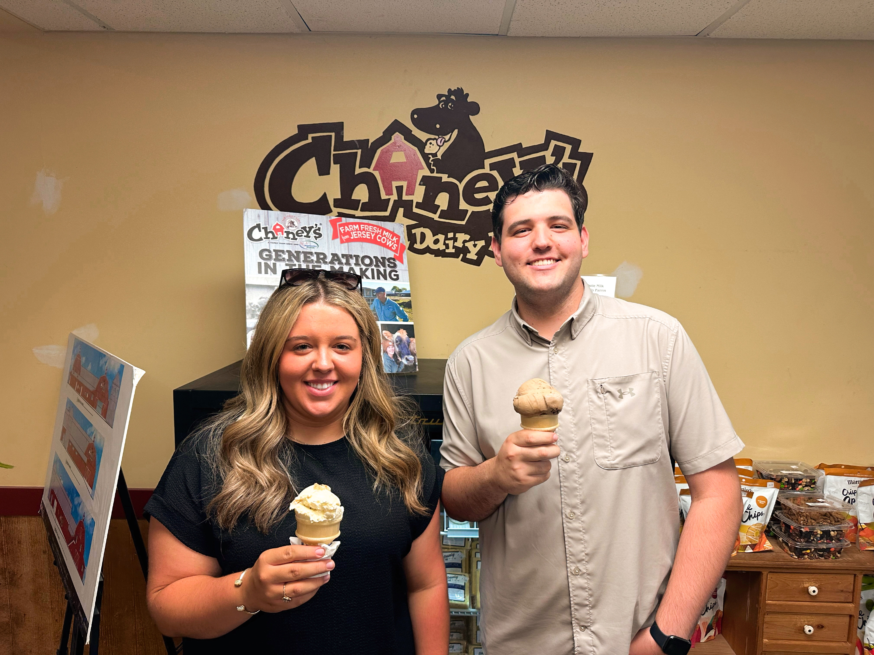 A young woman and a young man hold ice cream cones in front of a sign that says "Chaney's Dairy Barn."