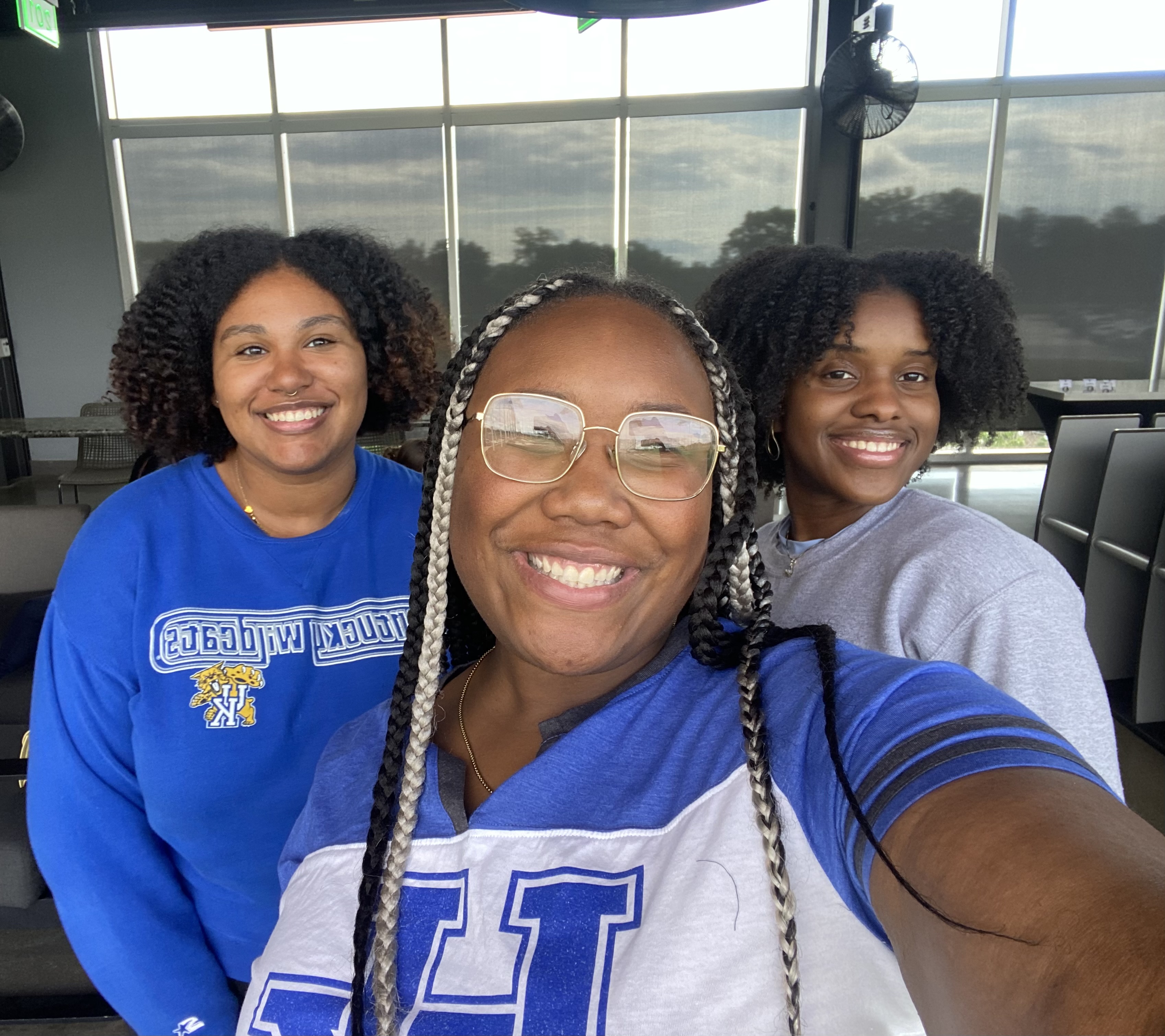 Three young women pose for a selfie. Two are wearing University of Kentucky apparel.